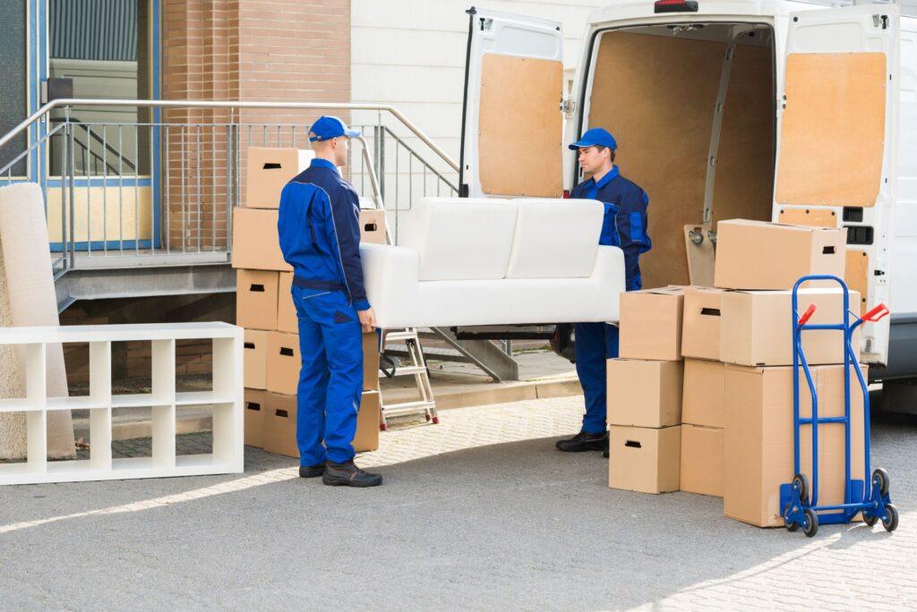 zwei umzugshelfer tragen ein sofa in ein gebaeude in arnsberg mit umzugskartons im vordergrund