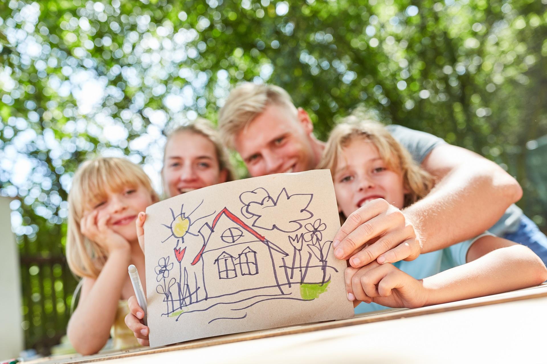 Familie zeigt bunte Hauszeichnung im Garten | Immobilienmakler Neustadt in Holstein