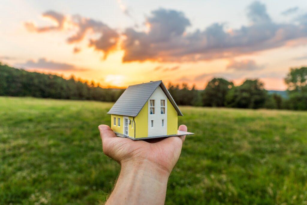 Hand hält Miniaturhaus im Sonnenuntergang | Immobilienmakler Neustadt in Holstein